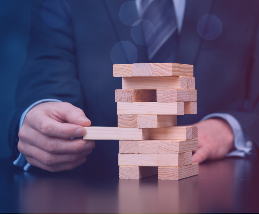 Risk Mitigation in Business Growth Business professional removing a wooden block from a stacked tower, symbolizing risk mitigation and stability